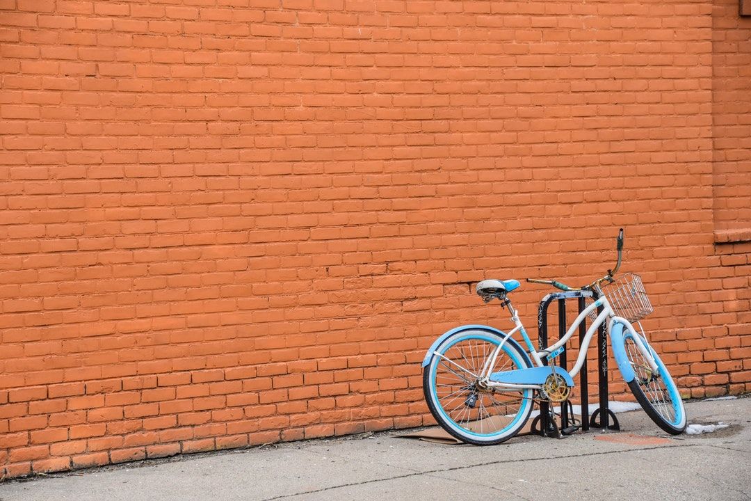 Light blue and white cruiser bicycle with a front basket parked against a bright orange brick wall